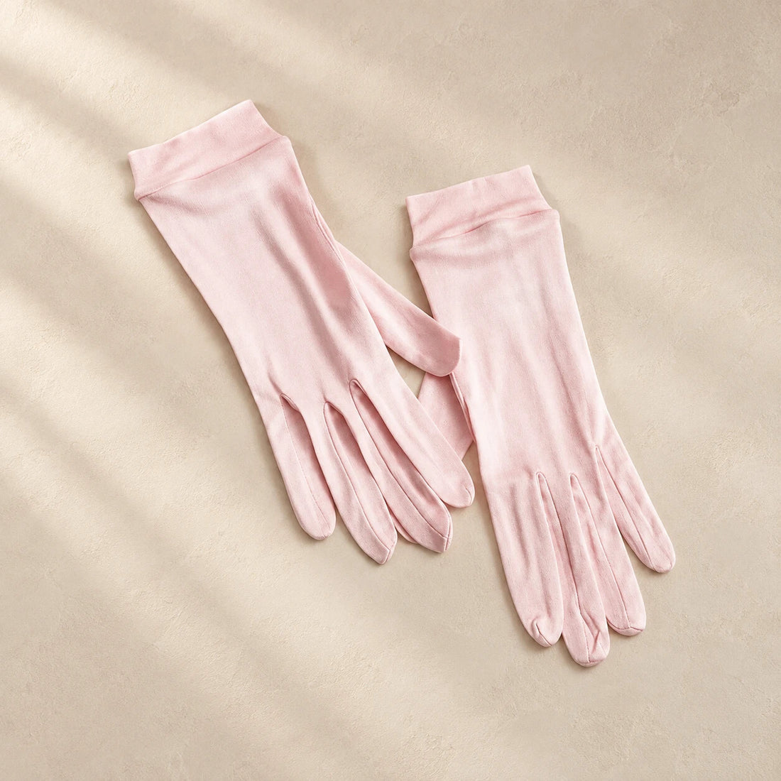 Blush silk sleep gloves on a warm neutral surface
